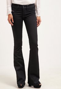 Pantalones vaqueros de tiro alto, de corte acampanado y color negro, confeccionados en denim, con bolsillos frontales, cremallera y detalles de costura sutiles.