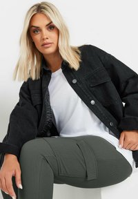 Svart denimjacka med tryckknappar, vit t-shirt under, och olivgröna ribbade byxor med fickdetaljer. Släta texturer och lager-på-lager look.