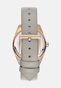 Het DKNY horloge heeft een lichtgrijze leren band, een roségouden metalen kast en een ronde wijzerplaat met een gepolijste afwerking en logo-detail op de sluiting.