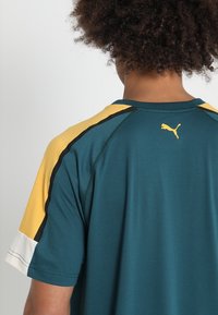 Puma sportstshirt i teal med gula och svarta accenter. Korta ärmar, rundad hals och en logotypdetalj på övre ryggen. Mjuk tygstruktur.