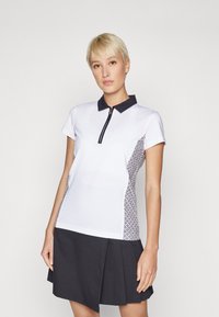 Polo shirt in white with a navy collar and zip, featuring patterned side panels. Material is smooth, with short sleeves and a relaxed fit.
