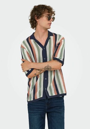 Camisa de punto de manga corta con rayas horizontales en verde, coral y azul marino sobre fondo blanco. Cierre frontal con botones y cuello.