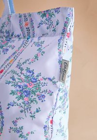 Šviesiai mėlyna rankinė, dekoruota rožių, violetinės ir žalios spalvų gėlių raštais, su maža etiketė, kurioje parašyta "Cath Kidston London."