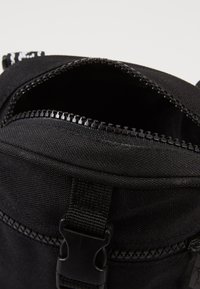 Zaino in tessuto nero con chiusura a zip superiore, caratterizzato da una tracolla resistente e una superficie leggermente texturizzata. Cuciture rinforzate lungo i bordi.