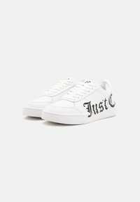 White sneaker with smooth synthetic upper, flat white laces, textured rubber sole, and large black "Just" graphic on the side.