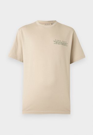 Μπλουζάκι μπεζ με κοντά μανίκια και στρογγυλή λαιμόκοψη, με μικρό πράσινο κείμενο "PURE ZEST" και ένα απόφθεγμα εμπνευσμένο από εσπεριδοειδή στο αριστερό στήθος.