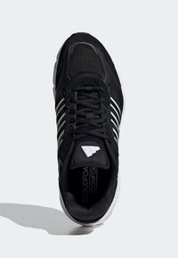 Svarta sportskor med ovan del av mesh och mocka, vita randdetaljer, vadderad krage och tjock svart sula. "CLOUDFOAM COMFORT"-etikett synlig.