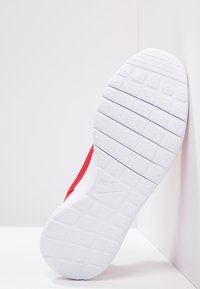 Červená sportovní bota s texturovaným svrchním materiálem a bílou gumovou podrážkou s vzorovaným designem. Logo je embosováno na podrážce.