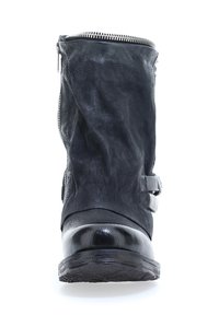 Botín negro hasta el tobillo con parte superior de cuero texturizado, puntera brillante, correas decorativas y un detalle de cremallera plateada en el costado.