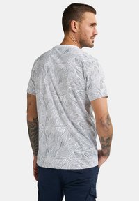 T-shirt med korte ærmer, der har en hvid base med sorte bladmønstre, lavet af blødt stof med en afslappet pasform og rund halsudskæring.