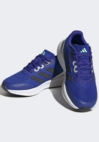 Scarpe da atletica viola con tessuto a rete, suole in gomma e tre strisce nere. Presentano un colletto imbottito e accenti blu-verdi sulla linguetta.