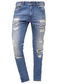 Vaqueros de mezclilla azul claro con un corte ajustado, que presentan detalles desgastados y múltiples rasgaduras, acentuando un aspecto usado. Diseño estándar de cinco bolsillos.