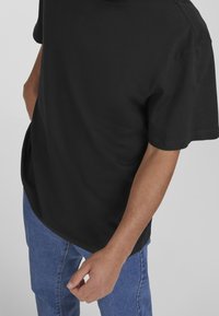 Black cotton t-shirt with short sleeves, round neckline, and a relaxed fit. Paired with light blue denim jeans.