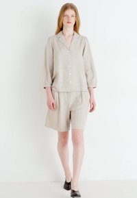 Completo in lino a due pezzi composto da una camicia con colletto e maniche a tre quarti, abbinata a pantaloni corti con cordoncino coordinati, in un colore beige chiaro.
