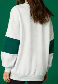 Jasnoszara oversize bluza z zielonymi kontrastującymi panelami na rękawach, plisowanymi mankietami i dołem, wykonana z miękkiej teksturowanej tkaniny.