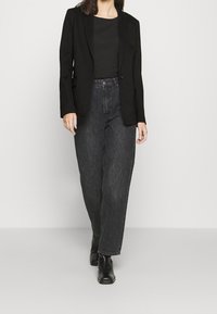 Czarna marynarka o dopasowanym kroju, noszona na czarnym topie, zestawiona z ciemnymi, wysokim stanem i prostymi nogawkami jeansami oraz czarnymi botkami za kostkę.