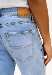 Lyseblå denimjeans med en sydd baklomme og en lærlabel med teksten "Tommy Jeans" nær linningen på en persons hofte.