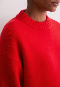 Czerwona sweter z dzianiny z ściągaczem przy dekolcie, luźnym krojem i miękką teksturą. Cechami wyróżniającymi są opuszczone ramiona oraz gładkie wykończenie materiału.