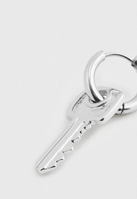 Stříbrně zbarvený kovový klíč připevněný na zavřeném kulatém kroužku na klíče, vystavený na jednoduchém světlém pozadí.