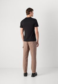 Tricou scurt negru, cu un design ajustat. Asortat cu pantaloni bej deschis, având buzunare la spate. Pantofi negri cu șireturi. Aspect simplu și curat.