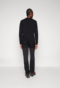Black long-sleeve shirt with a round neckline paired with black pants featuring contrasting textures. The person wears hiking boots.