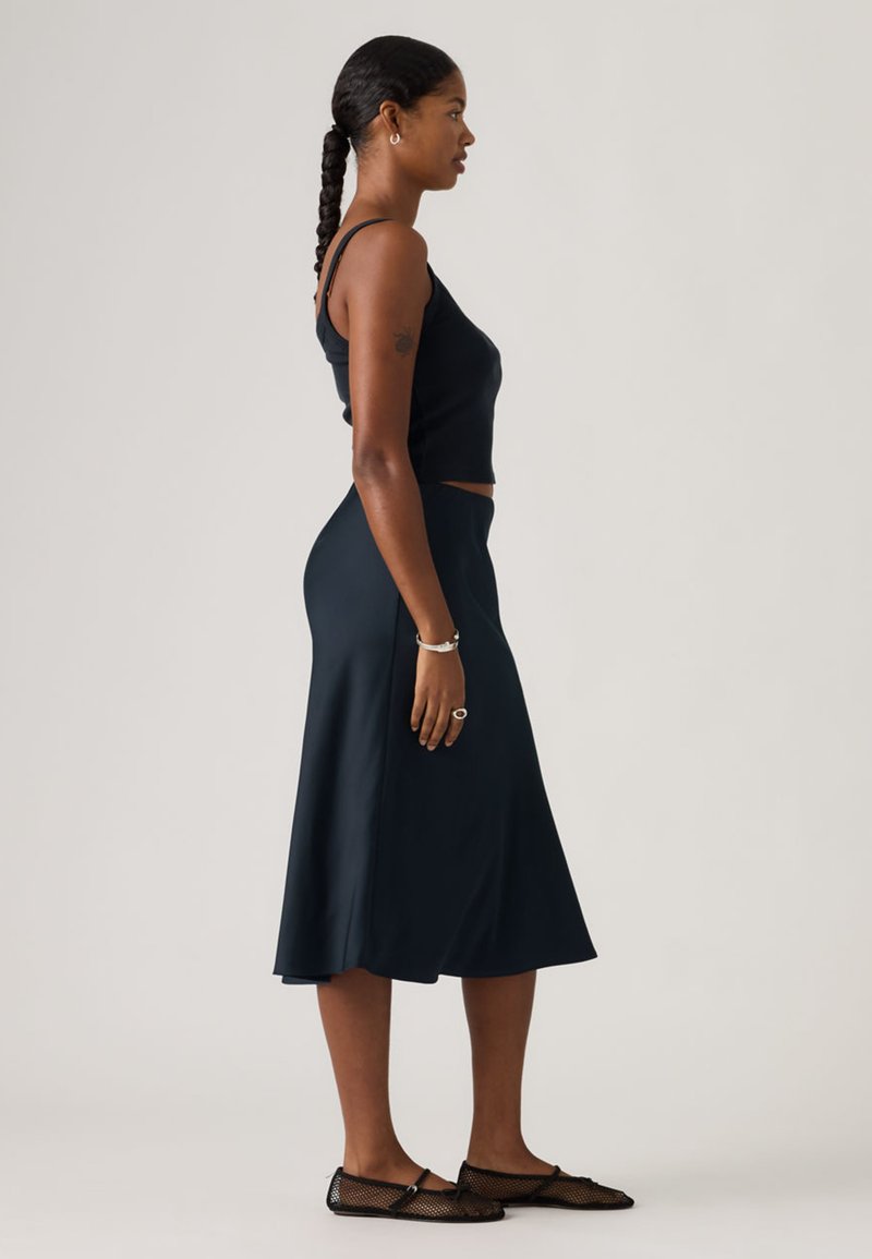 Black cropped tank top paired with a knee-length, flowing dark skirt. The model wears mesh flats and minimal silver jewelry.