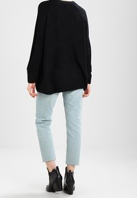 Schwarzer übergroßer Pullover mit strukturiertem Strick, kombiniert mit hellblauen, cropped Jeans und schwarzen Stiefeletten mit blockierendem Absatz.