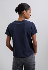 Camiseta de manga corta azul marino hecha de algodón, con cuello redondo y costuras visibles. Combinada con jeans grises.