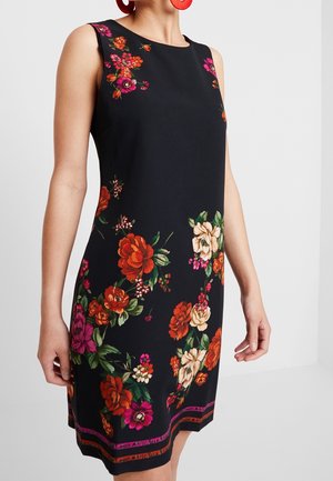 Czarna sukienka bez rękawów z żywymi wzorami kwiatowymi w kolorach czerwonym, różowym i kremowym oraz wielokolorowym obszyciem przy dolnym brzegu, noszona przez stojącą osobę.