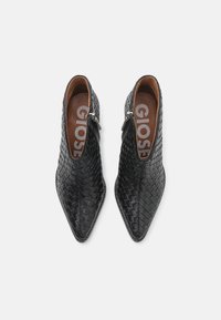 Botas de tobillo de cuero trenzado negro con punta afilada y cremallera lateral. El interior es marrón con la marca en la plantilla. Textura suave en toda la superficie.