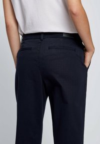 Marinblå byxor med en slät textur, som har en skräddarsydd passform, bakfickor och en logotyp på midjan.