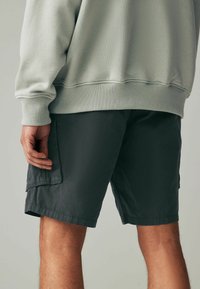 Grauer Baumwollpullover mit gerippten Bündchen, kombiniert mit dunkelgrauen Cargo-Shorts mit Seitentaschen und geradem Saum.