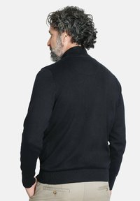 Suéter negro de punto con cuello alto y dobladillo acanalado. Tejido ligero, caracterizado por una textura suave y un ajuste entallado.