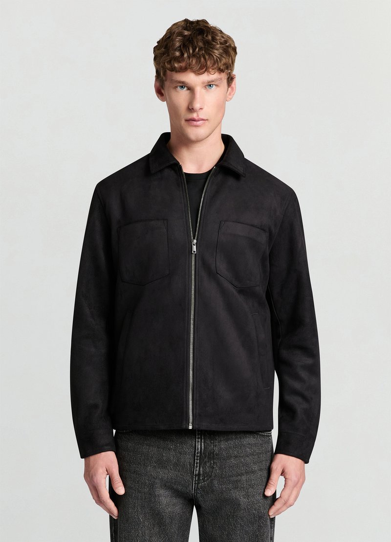 Veste en daim noir avec fermeture éclair à l'avant, petit col, deux poches poitrine et coupe décontractée. Finition texturée et palette de couleurs monochrome.
