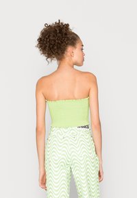 Top tubular smock verde com borda rizada, combinado com calças verdes de cintura alta com padrões ondulados brancos.