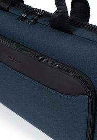Marineblauwe tas met een textuurstof buitenkant, voorzien van een zwarte rits en accenten, slank design en een voorvak met een gladde, matte afwerking.