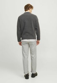Grauer Strickpullover mit geripptem Saum, getragen über einem weiß-hellgrau gestreiften Hemd, kombiniert mit hellgrauen Hosen und schwarzen Schuhen.