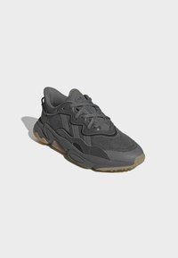 Dark gray sneaker with mesh and synthetic overlays, rounded toe, thick sole, and subtle textured accents. Laces and logo detail present.