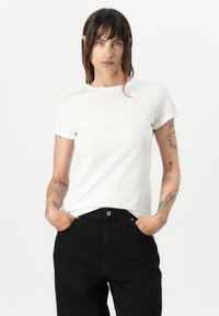 White short-sleeve t-shirt with rolled cuffs, made from cotton. Paired with black high-waisted pants featuring straight legs and front pockets.