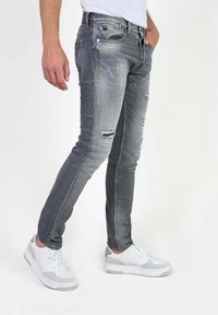 Verbleekte grijze denim skinny jeans met versleten details, voorzien van vijf zakken, een rits en een aansluitend ontwerp. Gecombineerd met wit-grijze sneakers.