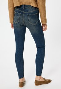 Jeans de mezclilla azul ajustados con cintura alta, dos bolsillos traseros y una textura suave, ligeramente descolorida, combinados con mocasines marrones.