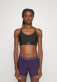 Melnas sporta krūšturis ar logo detaļām un sacīkšu aizmuguri, apvienots ar violetiem šortiem ar elastīgu jostu un zīmola nosaukumu.