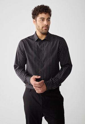 Black long-sleeve shirt with thin vertical stripes in gold. Features a button-down front and standard collar. Smooth fabric texture.