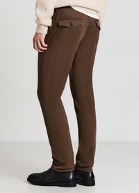 Braune Hosen aus weichem Stoff mit schmaler Passform, Gesäßtaschen mit Knopfverschluss und einfachem Saum. Getragen mit schwarzen Lederstiefeln.