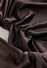 Elastični materijal tamno smeđe boje s glatkom teksturom, s naborima i suptilnim tkanim uzorkom.