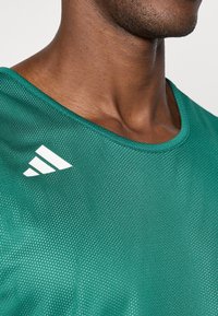 Zelený, ľahký atletický dres s sieťovinou, s okrúhlym výstrihom a bielym logom Adidas na ľavom pleci.