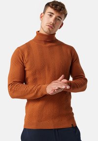 Pull à col roulé en orange brûlé, présentant un motif en zigzag texturé et des poignets côtelés. Fabriqué à partir d'un matériau doux et extensible.