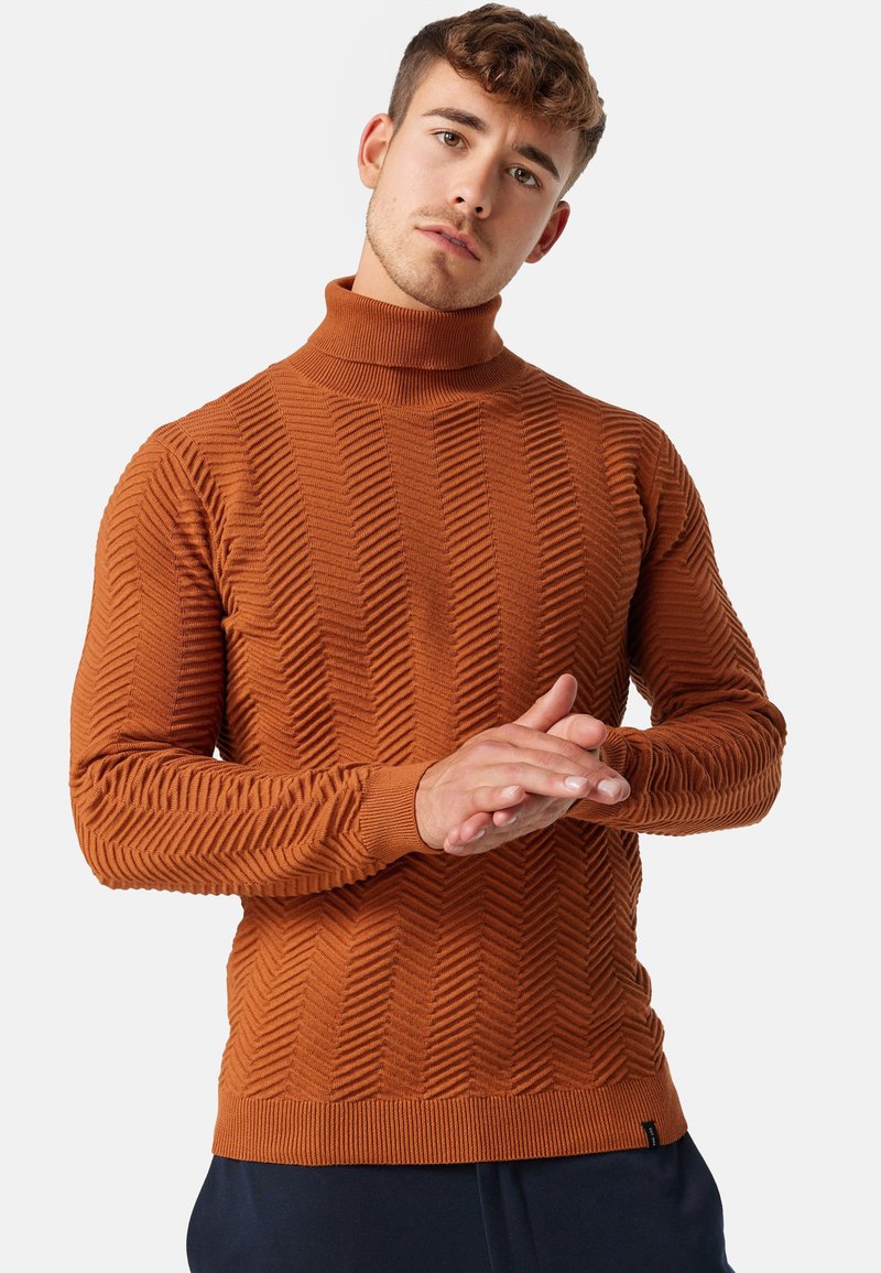 Pull à col roulé en orange brûlé, présentant un motif en zigzag texturé et des poignets côtelés. Fabriqué à partir d'un matériau doux et extensible.