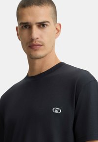 T-shirt blu scuro in morbido cotone, con collo tondo, maniche corte e un piccolo logo bianco sulla parte sinistra del petto.