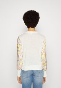 Biały, lekki sweter z wzorzystym materiałem w pastelowych kolorach na rękawach, z żebrowanym kołnierzem i mankietami.